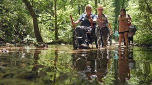 Park Ranger Katie Corrigan helps Carly Peterson, ADA coordinator for Knox County and volunteer for Catalyst Sports, navigate a creek crossing on Cooper Road Trail. Photo provided by Jim Matheny, Friends of the Smokies. 